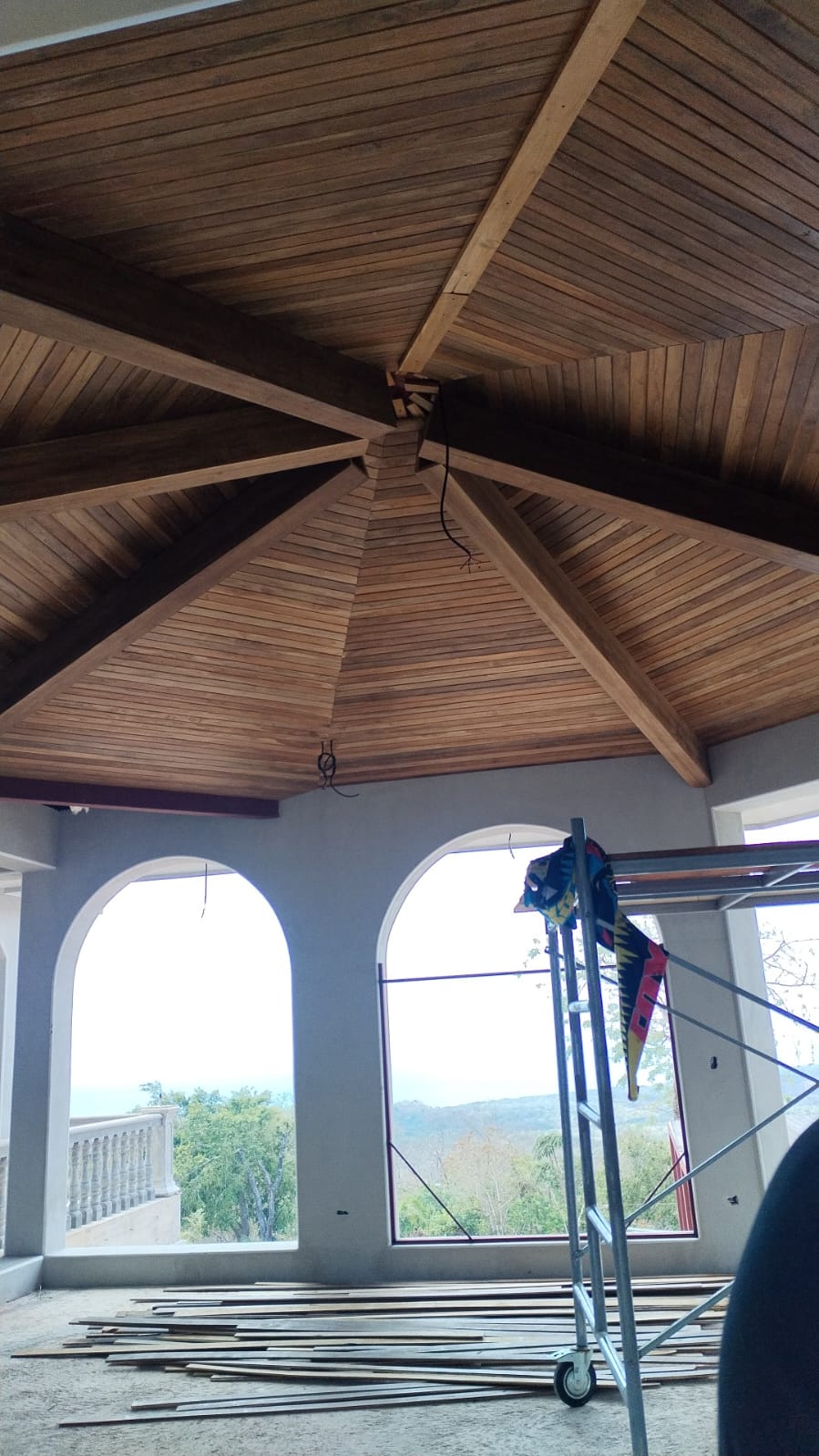 Vista interior de una construcción con un techo de madera abovedado y ventanas arqueadas.