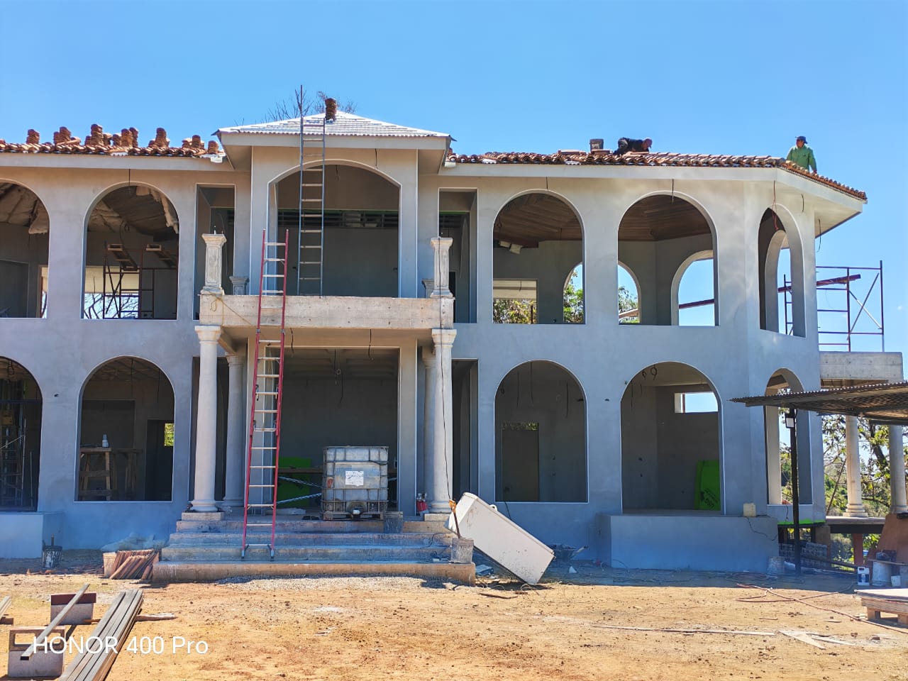 Se observa una casa de dos pisos en construcción con trabajadores instalando tejas en el techo.