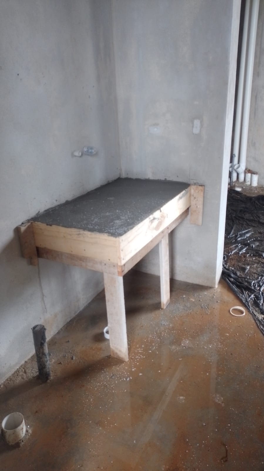 Se observa una estructura de concreto en proceso de construcción con encofrado de madera en una habitación en obra gris.