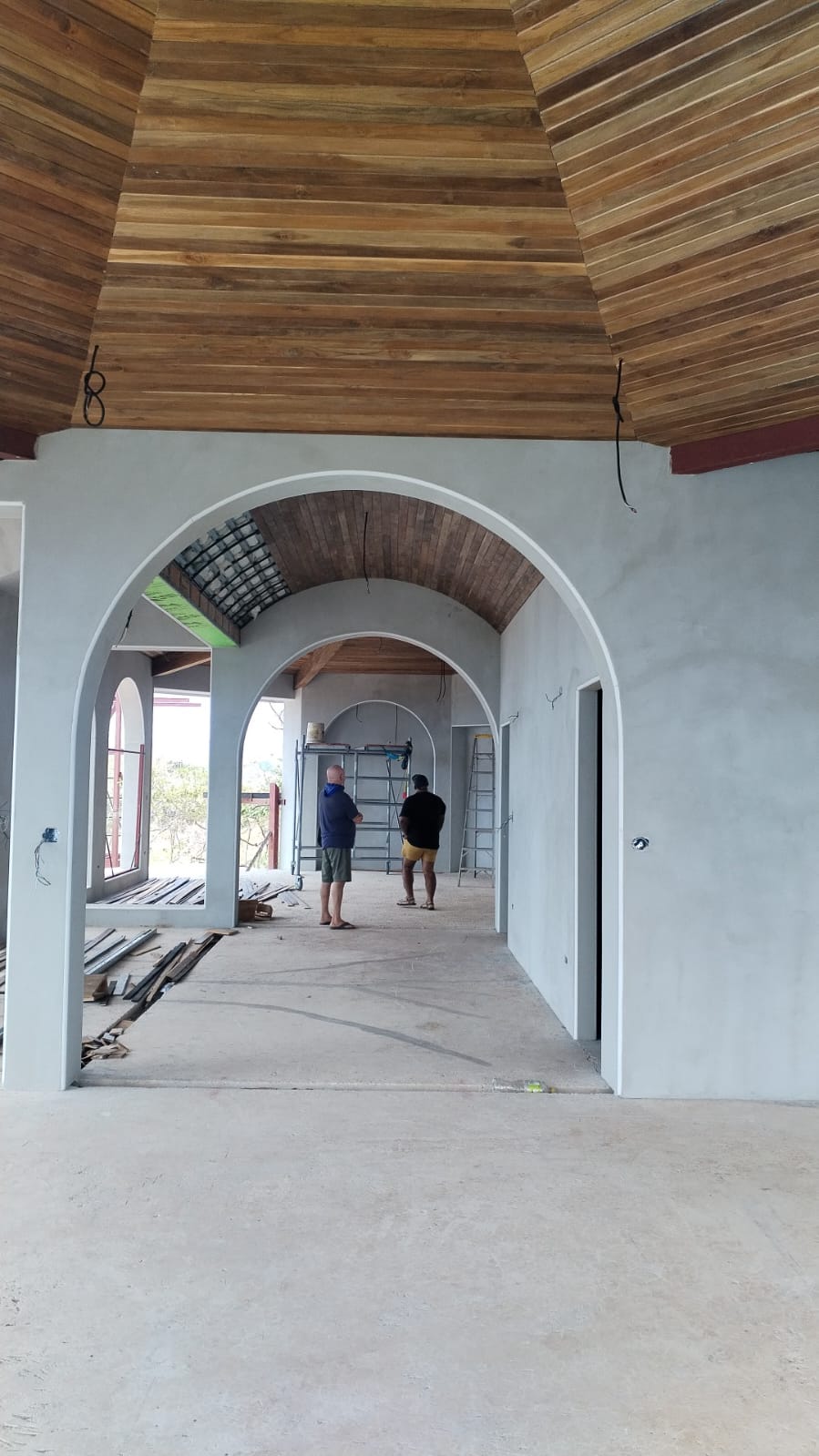 Dos personas inspeccionan una construcción en proceso con arcos de concreto y techos de madera.