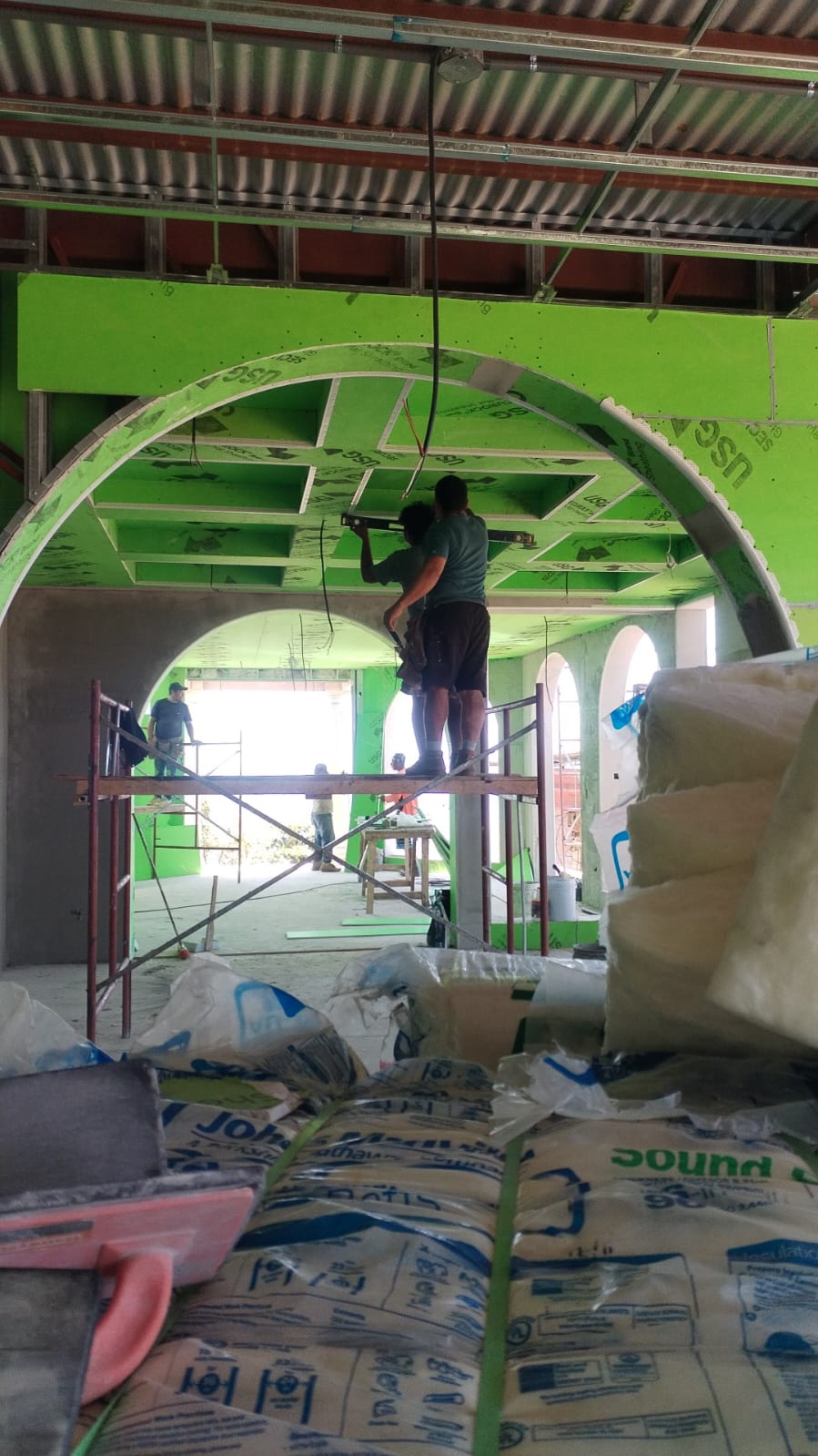 Trabajadores de construcción instalan paneles de yeso verde en una estructura de techo arqueado.