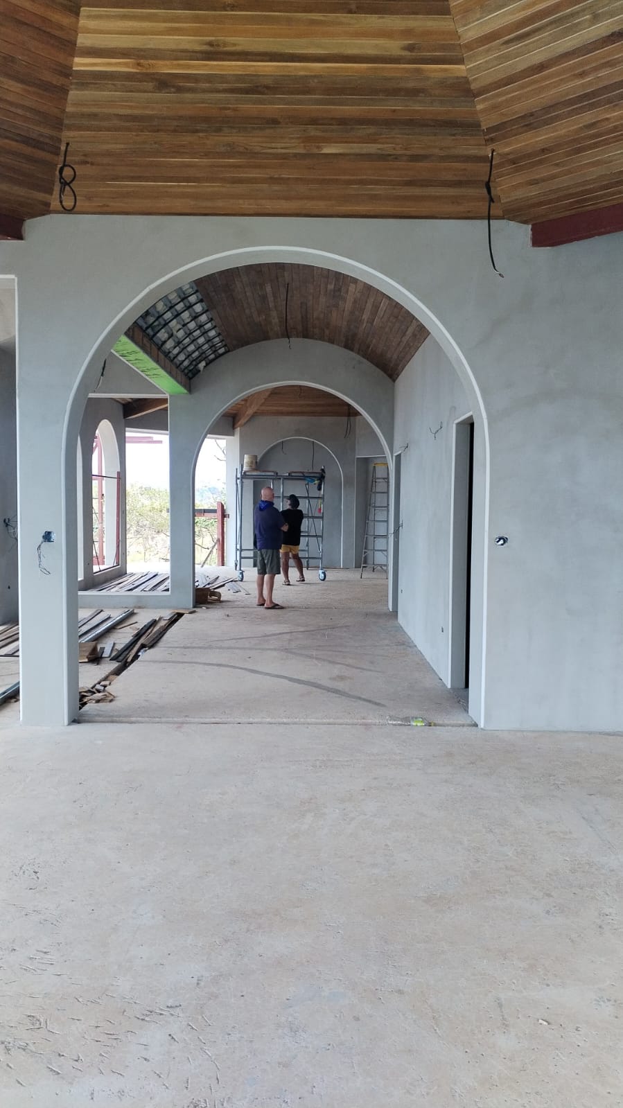 Vista interior de una construcción en proceso con arcos de concreto y techos de madera.