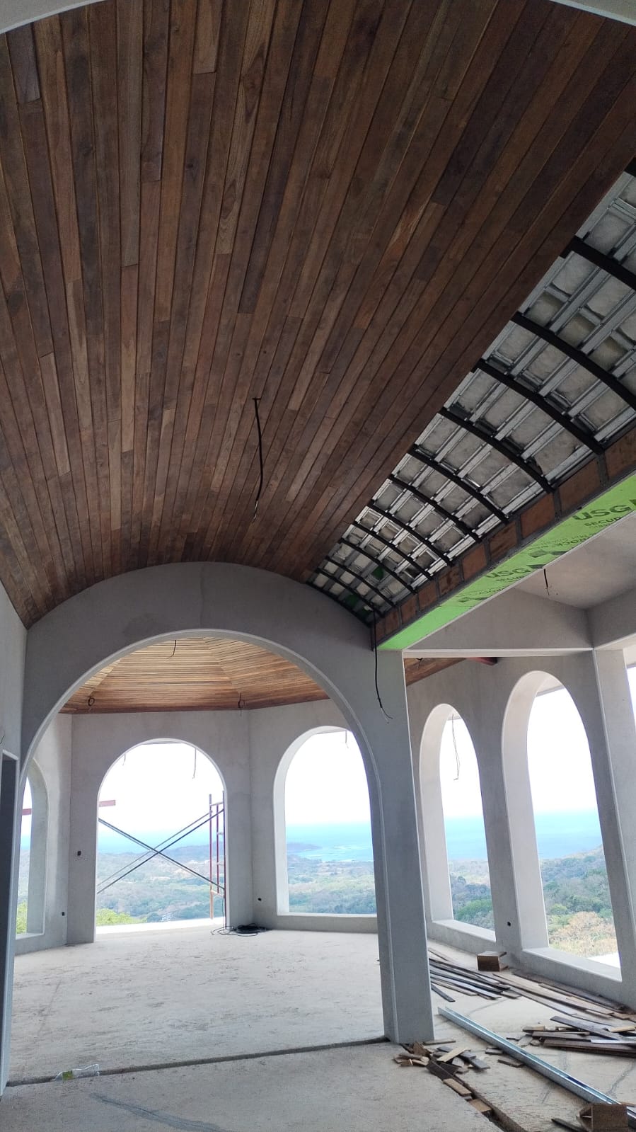Vista interior de una construcción en proceso con techos de madera y arcos que muestran una vista panorámica.